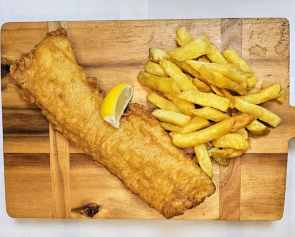 Battered Cod and Chips in a box with a lemon wedge laid out on a wooden board